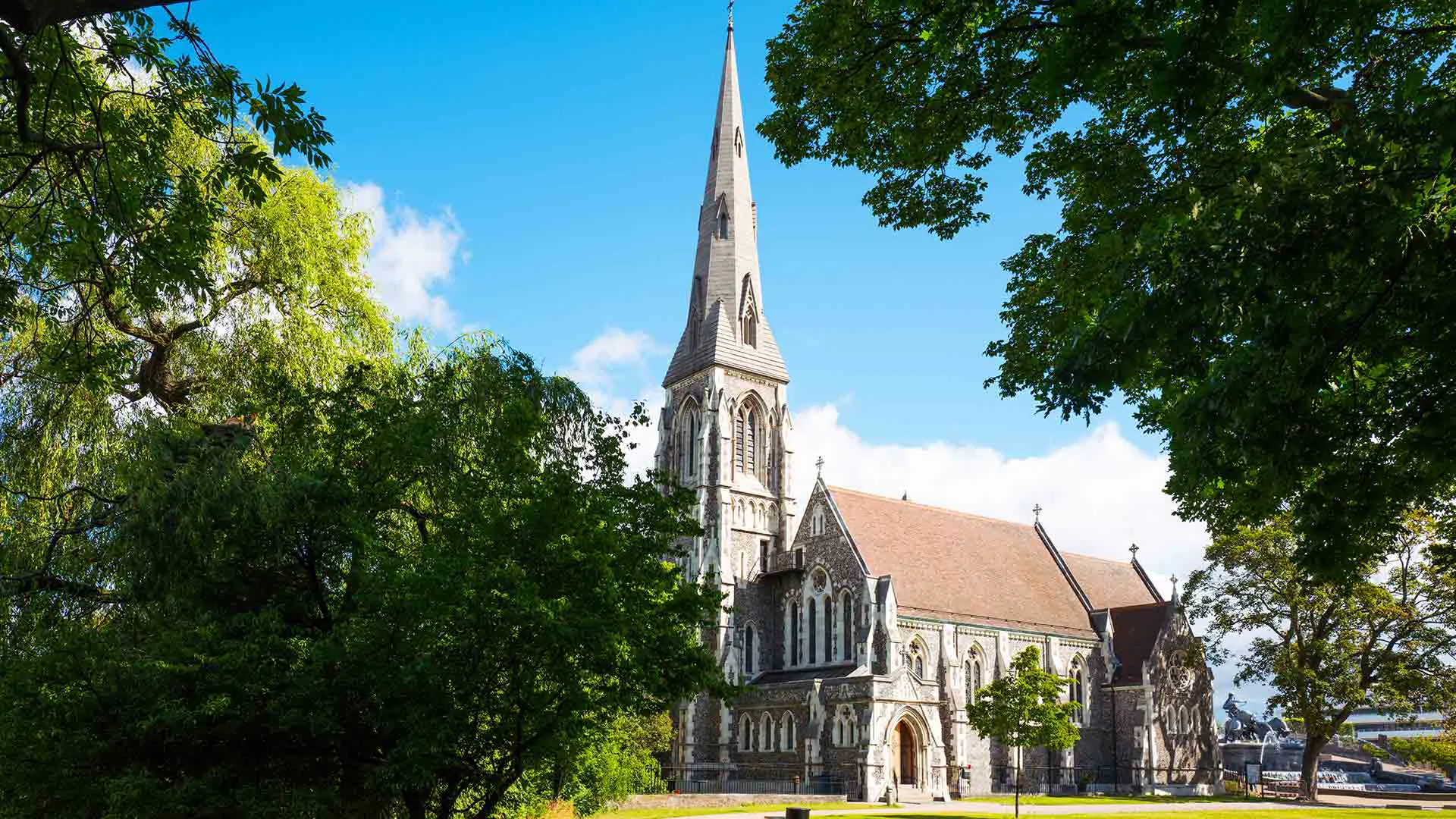Light stone church with tall steeple surrounded by trees