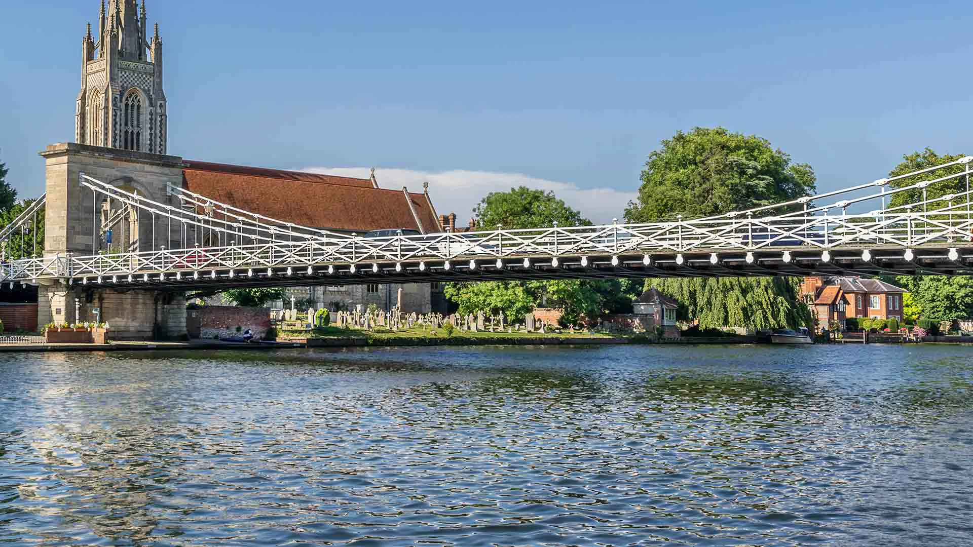 White suspension bridge over river with church and graveyard