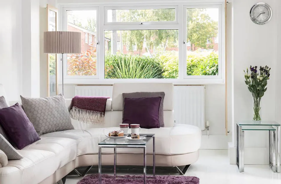 White leather sofa with purple pillows and a view of trees outside