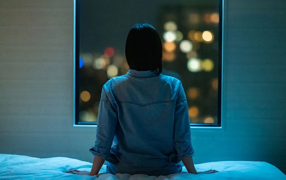 Person sits in hotel room looking out window at night