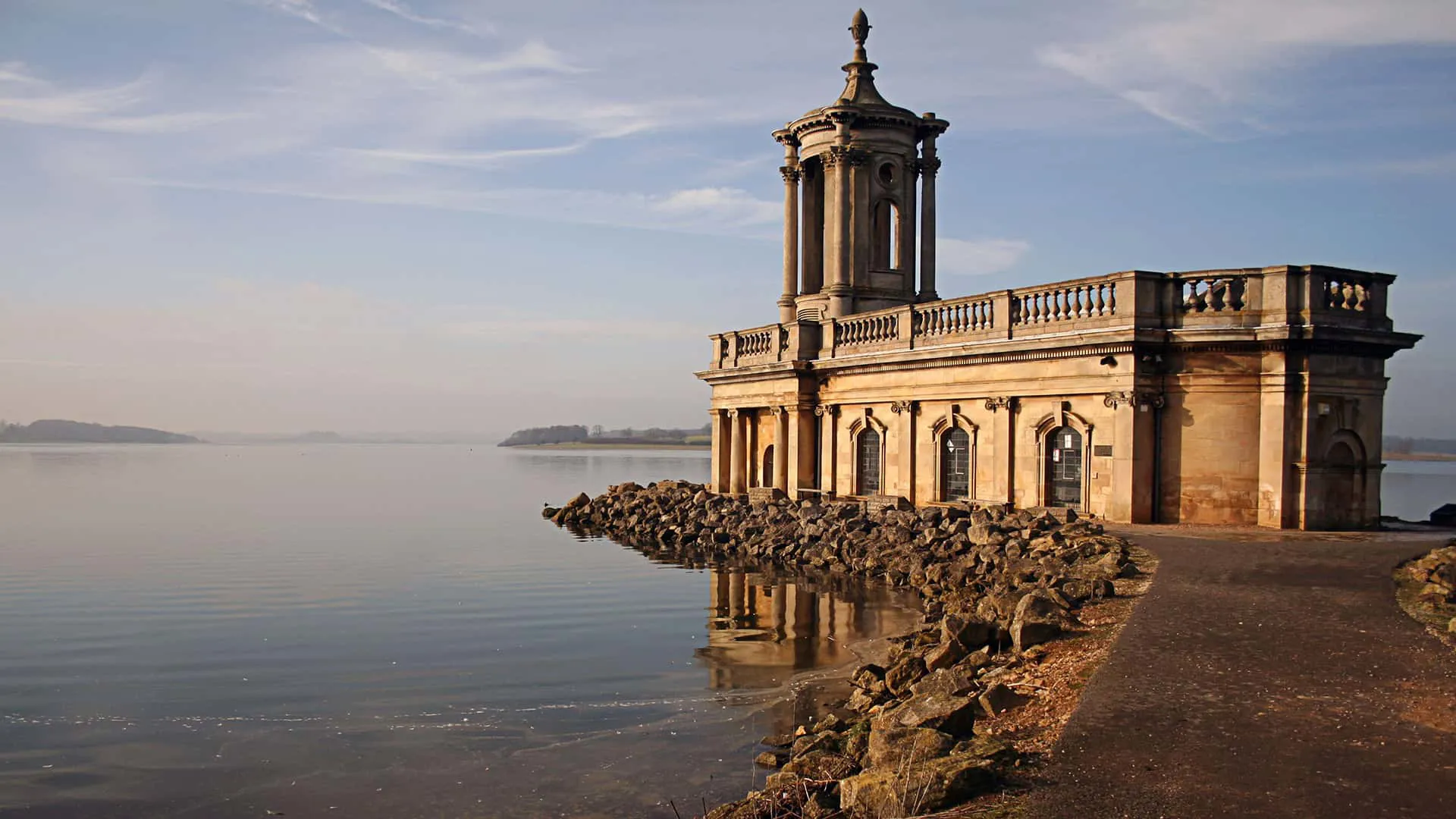 Light stone building by lake reflecting sunlight