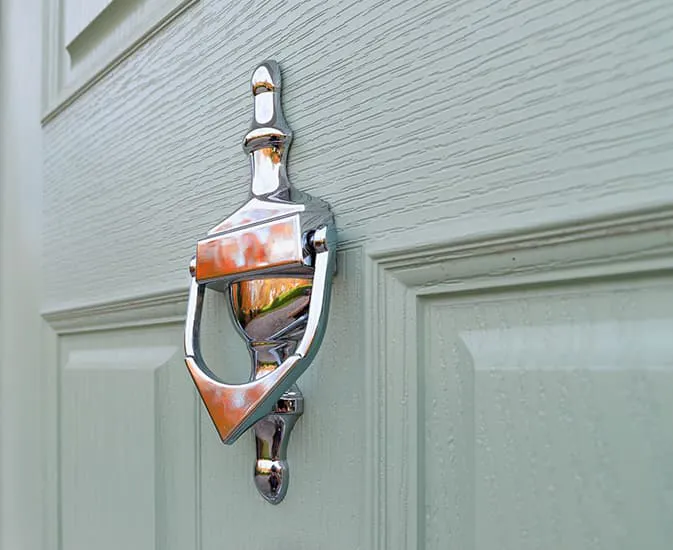 Silver door knocker on light sage green door