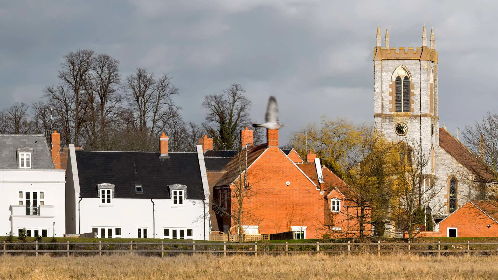 Houses with brick and dark roofs next to a church tower