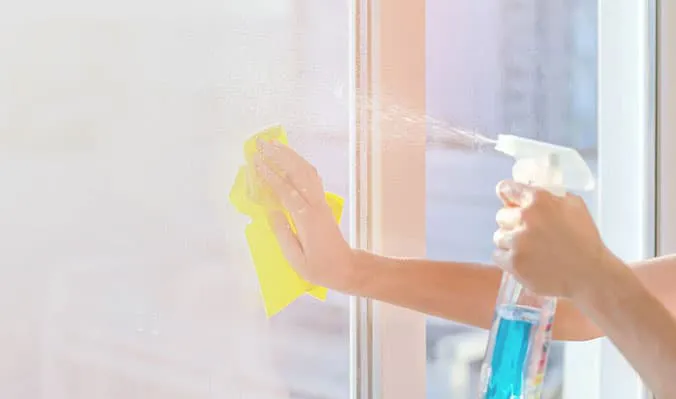 Person cleaning window with yellow cloth and spray bottle