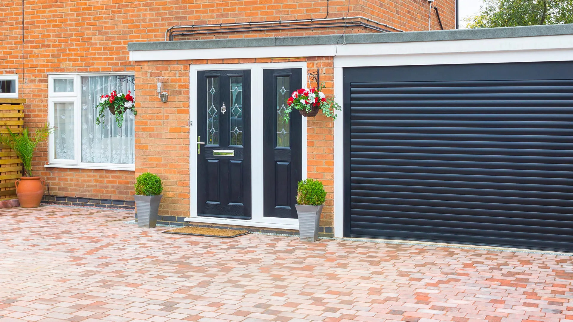 Brick house entrance with black door and paved driveway