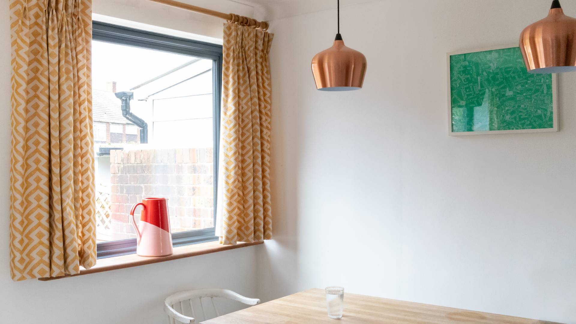 Yellow patterned curtains by window with red pitcher and copper pendant lights