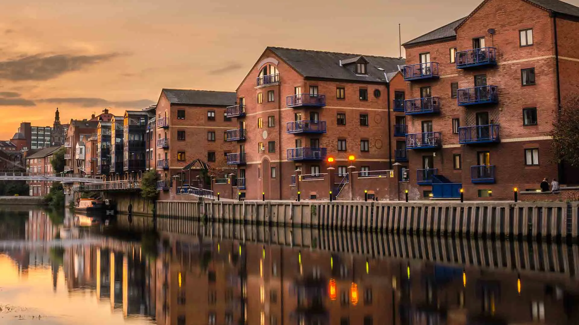 Brick buildings reflecting on calm river water at sunset