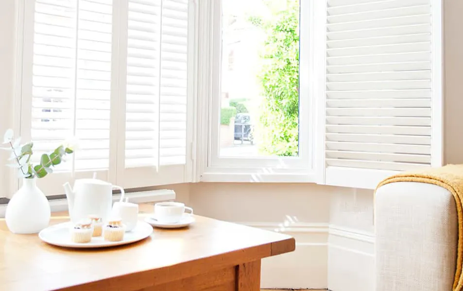 White shutters on a bay window with teacups and cupcakes