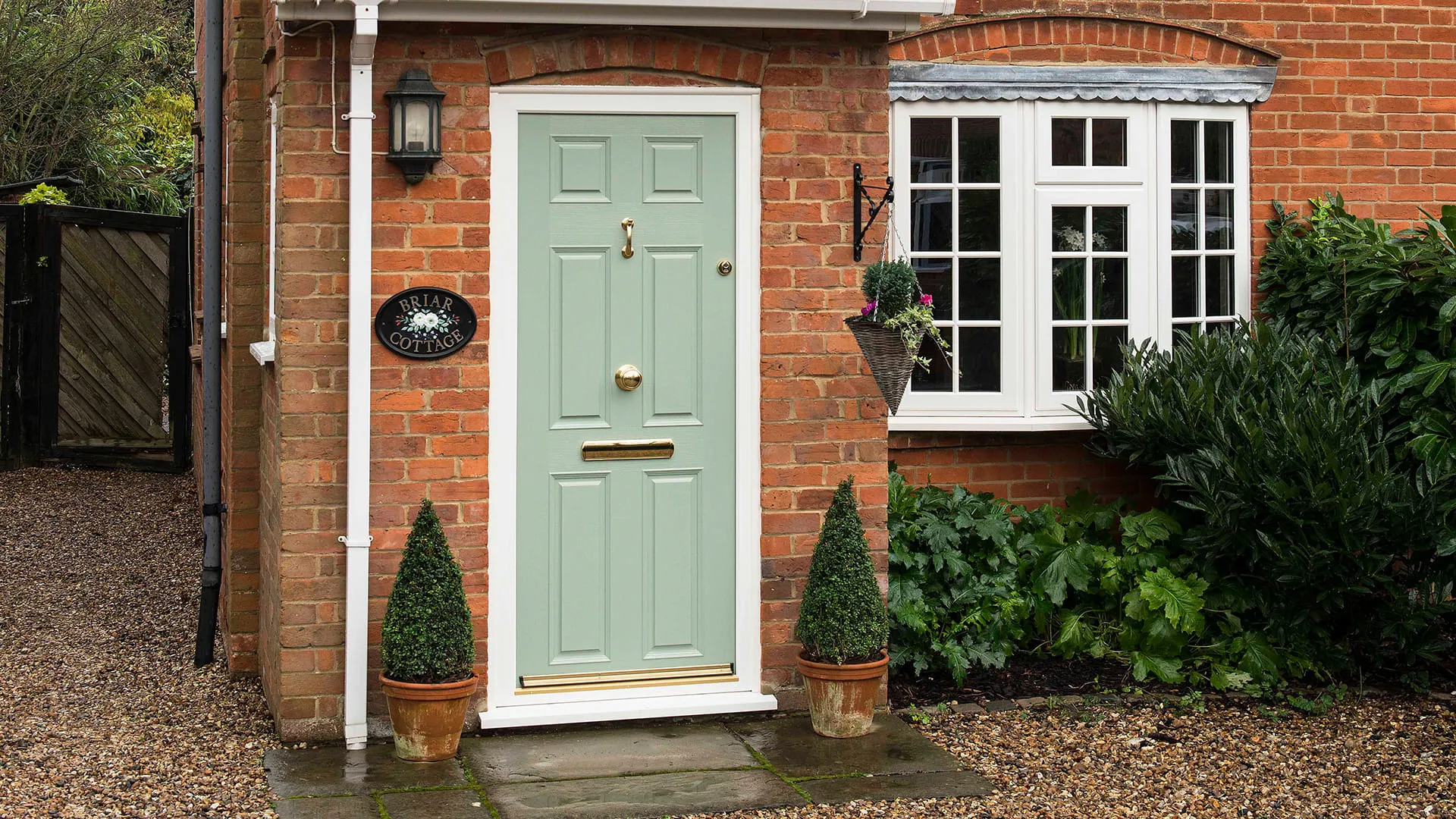 Sage green door on brick house with potted topiaries