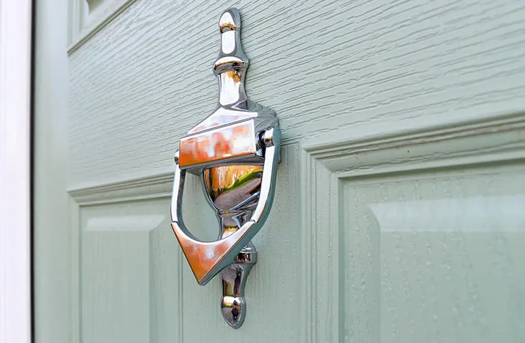 Silver door knocker on a light sage green door