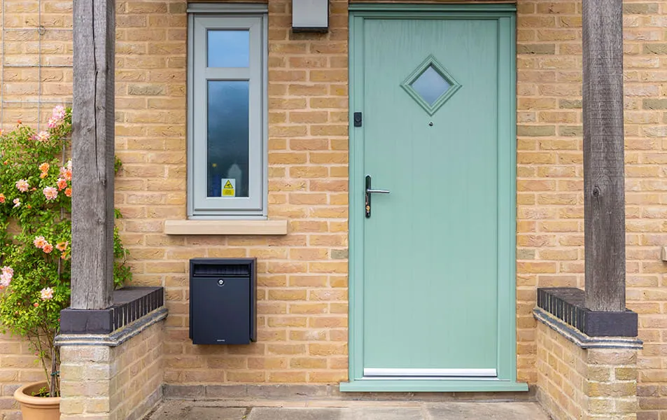 Light sage green door with diamond window on a house of beige bricks