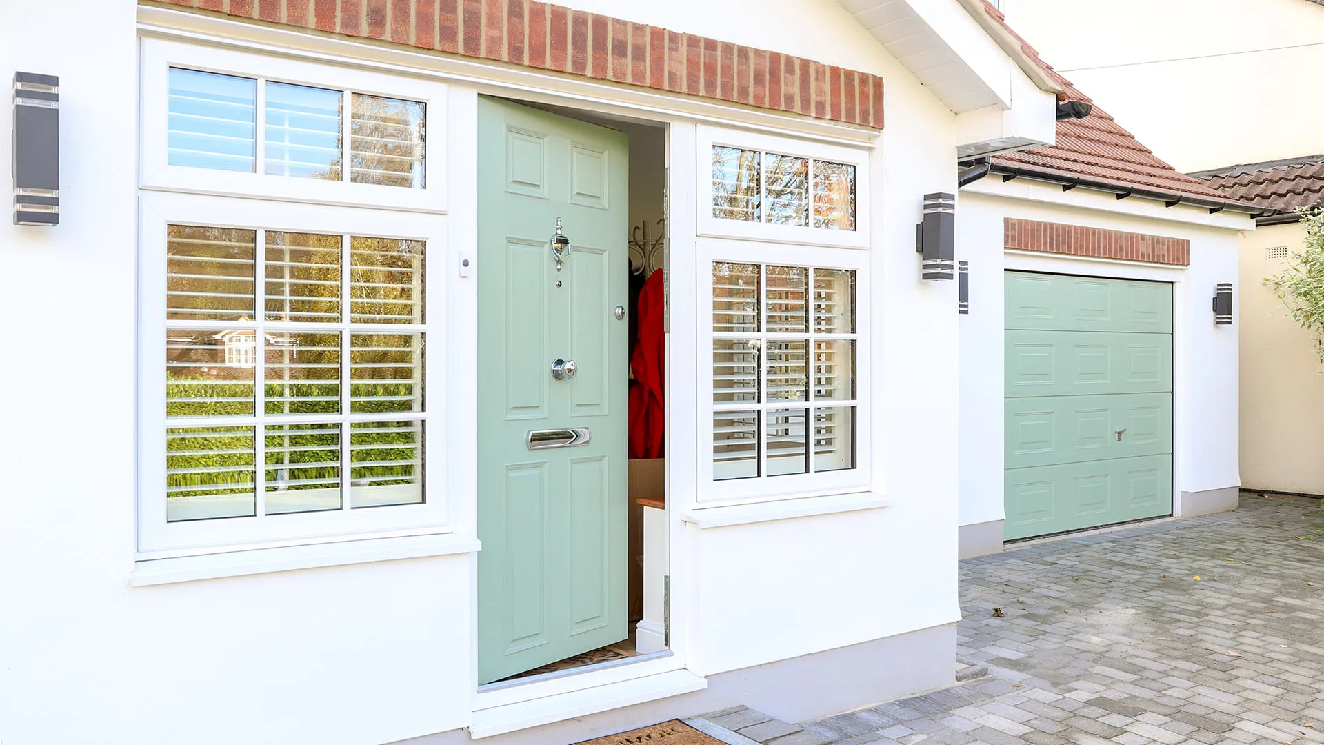 Light sage green door with white window frames and a light gray driveway