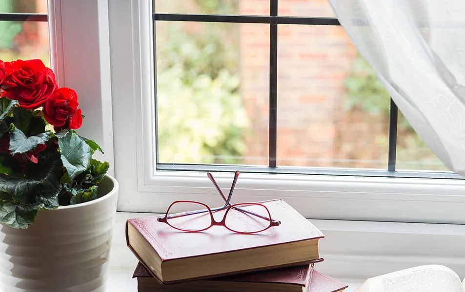 Red eyeglasses on stack of red books by window with flowers