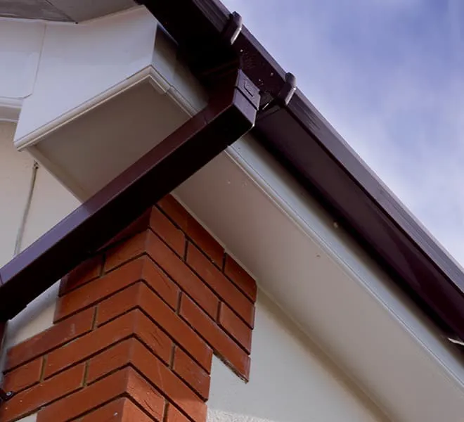 Dark brown gutters and white fascia board on a red brick house