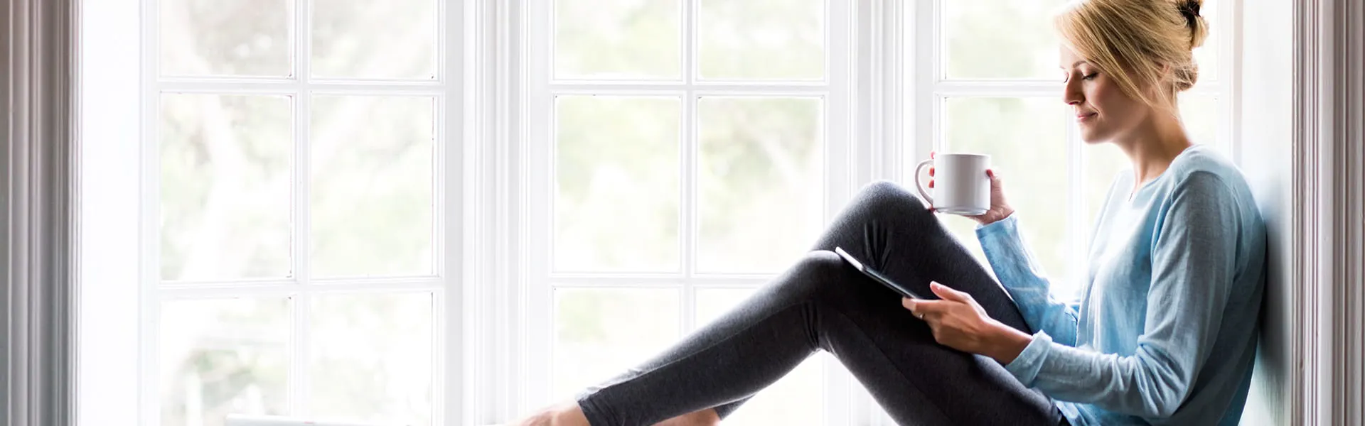 Woman relaxing by window with coffee and tablet