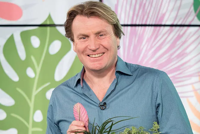 Man smiling holding a pink plant leaf