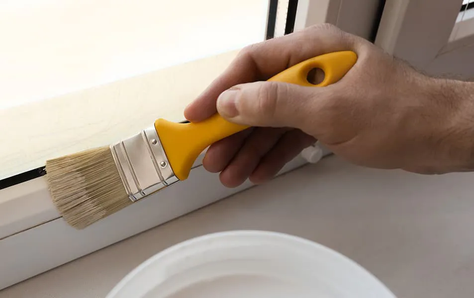 Hand painting window frame with a yellow handled paintbrush