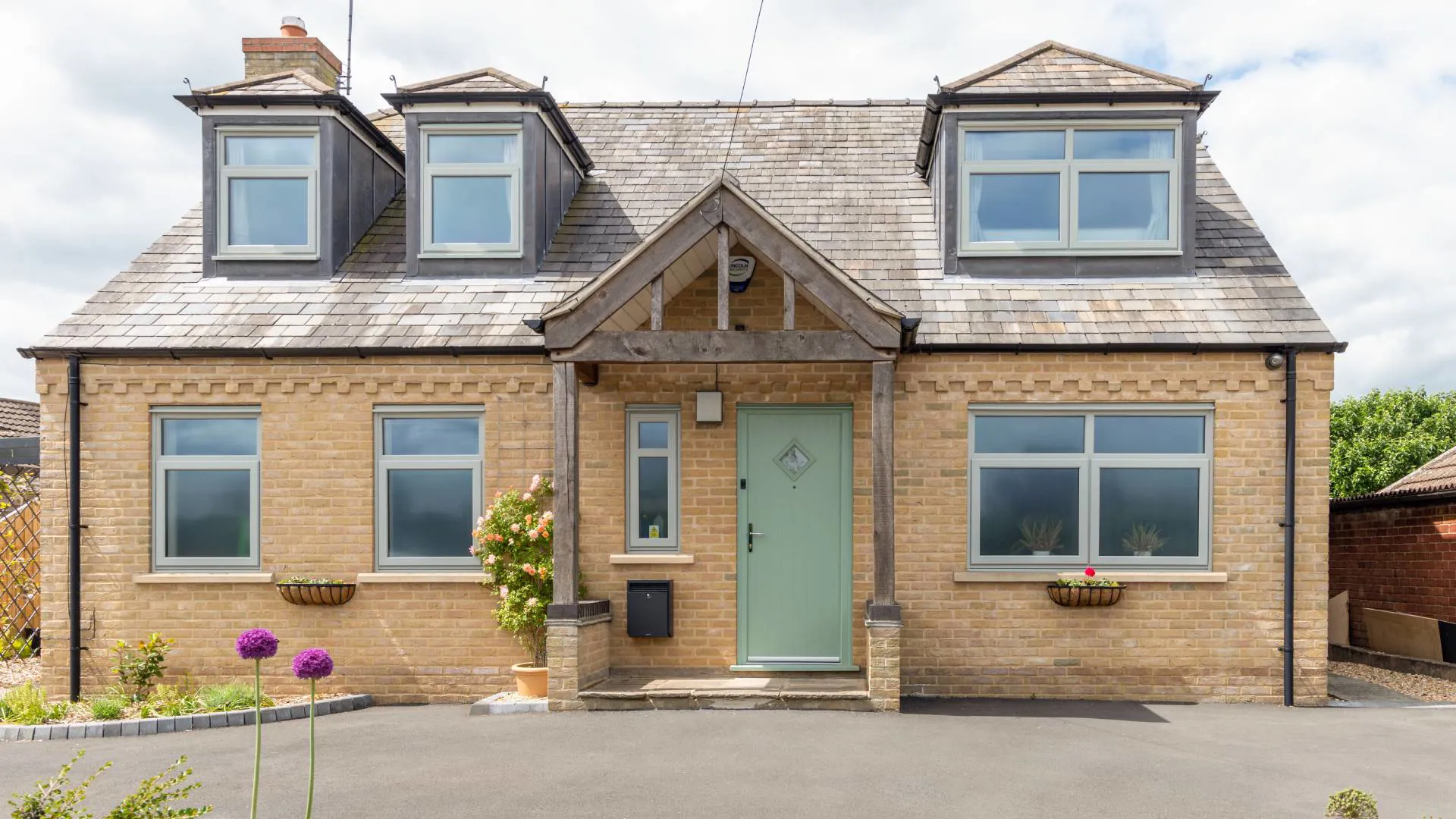 Light beige brick house with sage green front door and light grey windows