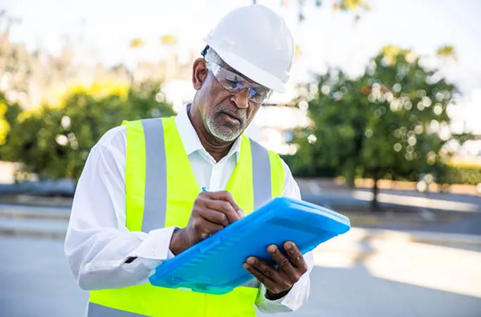 Person in safety vest writing on clipboard