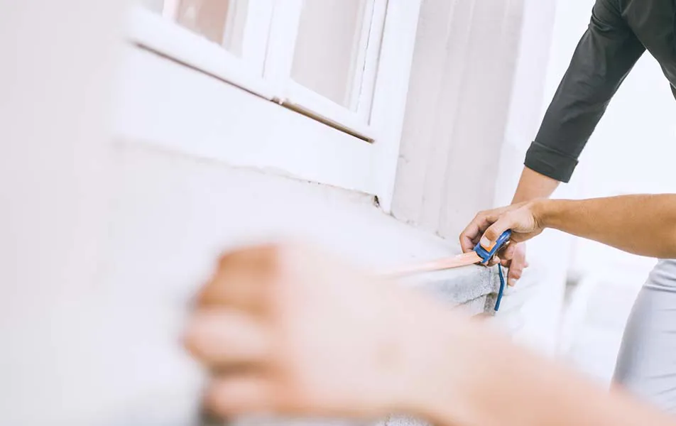 Person measuring with a tape measure on a house wall