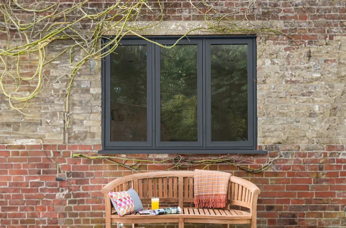 Dark gray Everest conservatory window with brick wall and wooden bench