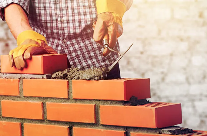 Person building a brick wall with mortar