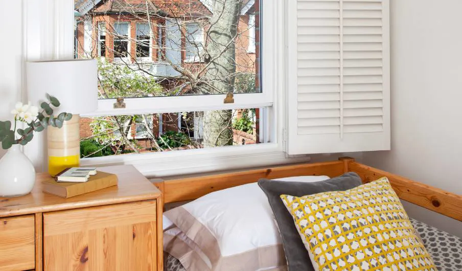 Wooden bedroom with white window shutters and yellow patterned cushions