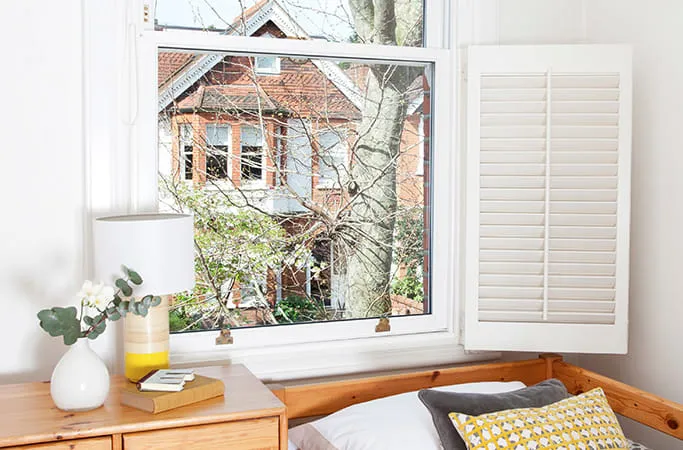 White window with shutters and view of red brick house